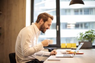 Man Holding Teacup Infront Of Laptop On Top Of Table Inside 925786