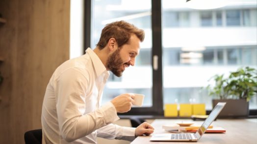 man holding teacup infront of laptop on top of table inside 925786