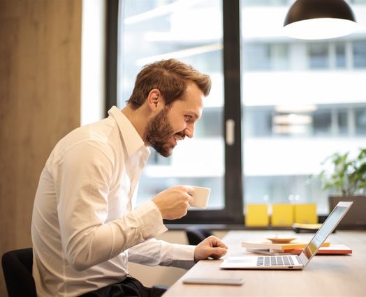 man holding teacup infront of laptop on top of table inside 925786