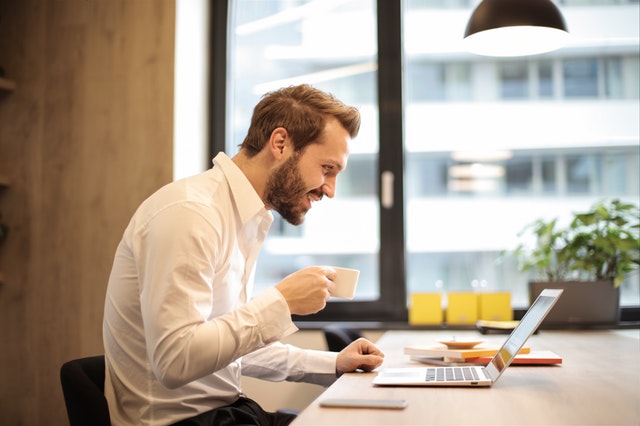 man holding teacup infront of laptop on top of table inside 925786