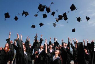 Newly Graduated People Wearing Black Academy Gowns Throwing Hats Up In The Air